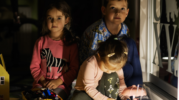 Barn som sitter i mørket med en lampe foran seg.